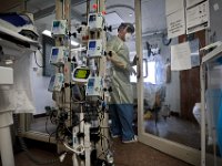 Dr. Michael Barretti, walks into a sealed room containing a COVID-19 patient in critical condition at the St. Luke's Hospital ICU in New Bedford, MA. Each of the different computing devices controls a specific medication. Normally these interfaces would be found inside the room, but for greater ease in operating them, they are now seen outside the sealed room. PHOTO PETER PEREIRA