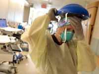 Miriam Hinojos, RN, places her safety gear on again, before checking in at a COVID-19 patient in the Wilkes Wing at St. Luke's Hospital in New Bedford.  The equipment is either disposed of completely or cleaned after every session. PHOTO PETER PEREIRA