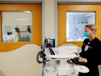 Respiratory therapist, Cassidy Gomes, fills in her patients profile, while inside the room a nurse can be seen monitoring a COVID-19 positive patient in the CCU at the Charlton Memorial Hospital in Fall River.  PHOTO PETER PEREIRA