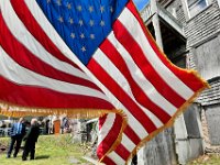 An American flag waves in the breese as James Reed, executive director of the Veterans Transition House, speaks with Bruce Portas in front of the building seen on the right, which will be called the SFC Bruce Portas Transitional Housing Center, during the groundbreaking ceremony held in New Bedford. [ PETER PEREIRA/THE STANDARD-TIMES/SCMG ]