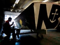 Edwin Arvelo, 16, puts the final touches on paintings that he and fellow New Bedford High School students made on  the side of the boat that they built under the guidance of the Community Boating Center, in the marine workshop at their school. [ PETER PEREIRA/THE STANDARD-TIMES/SCMG ]