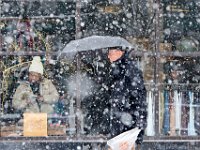 A man with umbrella in hand walks past The Madlita in downtown New Bedford, MA as snow continues to fall, while inside a woman takes a look at a pair of shoes on sale.  [ PETER PEREIRA/THE STANDARD-TIMES/SCMG ]