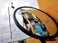 Jim Tripp, owner of Davis & Tripp Marina, is reflected on the mirror of the crane that he is operating to lift Dustin Lavalley up to the top of the mast in order to install the wind vane, on the sailboat they are rigging at the Dartmouth marina.  [ PETER PEREIRA/THE STANDARD-TIMES/SCMG ]