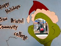 A woman walking up William Street in downtown New Bedford, MA fights the driving rain with umbrella in hand, as seen through the Grinch cutout installed in the Community Room of the lower lever at the Bristol Community College downtown Campus for a future holiday event, where students can put their face inside to take photos as the Grinch.    [ PETER PEREIRA/THE STANDARD-TIMES/SCMG ]