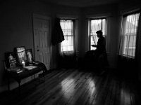 An undocumented man living in a home in New Bedford, looks out the window waiting for a ride to arrive.  In the corner a religious shrine can be see with a candle perpetually lit.    [ PETER PEREIRA/THE STANDARD-TIMES ]