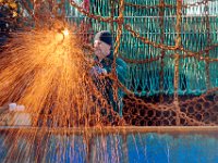 A fisherman sparks things up as he repairs the dredges aboard a scalloper docked in New Bedford harbor.   [ PETER PEREIRA/THE STANDARD-TIMES ]