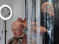 Sandro Quiles, owner, is seen behind the temporaty partitions that he had erected inside of his new Upper Kutz barber shop on Purchase Street in New Bedford, as he gives Tom Brown a haircut.