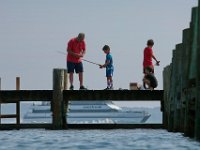 A man helps some youngsters with the bait on their line, as they enjoy a morning of fishing from a pier in the south end of New Bedford.  In the distance the Seastreak high speed ferry can be seen making it's way to Martha's Vineyard.