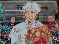 Two patrons of The Baker in downtown New Bedford flank a holiday themed baker painted on the windows of the downtown artisanal baked goods eatery, as they enjoy a snack.