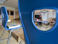 New teacher, Courtney Lima, is seen through the gap of one of the chairs placed on top of the desks in her classroom, which will not be occupied all year.  Courtney Lima who attended the Taylor School in New Bedford from K-6th grade as a student, returns for her first day of school, this time as a third grade teacher and this year will be teaching the Distance Learning Academy students who opted to stay home this school year.  PHOTO PETER PEREIRA