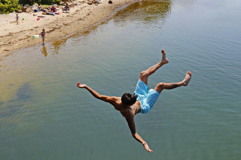 Eric Tavares stays cool by jumping off of a bridge crossing Little River in Dartmouth, MA PHOTO PETER PEREIRA