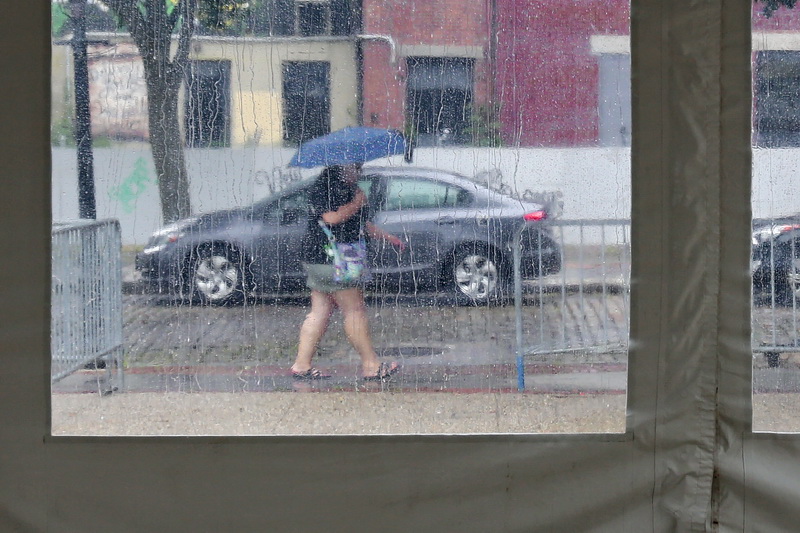 Rain runs down the plastic windows of a tent ready for the New Bedford Folk Festival at Custom House Square, as a woman walks past with umbrella in hand, fending off the heavy rain making its way across  the region.  PHOTO PETER PEREIRA