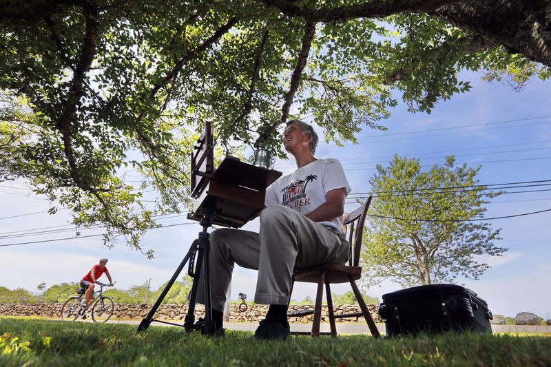 Scott Howard paints a scene with oil colors as cyclist makes his way past on Horseneck Road in Westport, MA.  PHOTO PETER PEREIRA