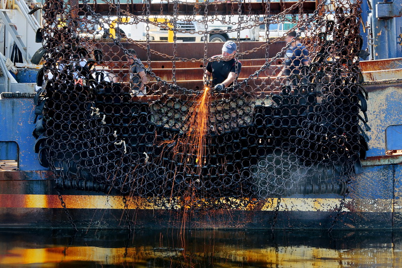 A fisherman sends sparks flying as he makes repairs to the dredges of the scalloper Santa Isabel docked in New Bedford, MA. PHOTO PETER PEREIRA