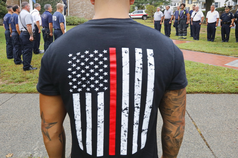 New Bedford firefighters and police officers stand at attention in the background as off duty New Bedford firefighter Derek Santos, joins them at a ceremony in remembrance of the events of 9/11 in front of the Lawler Library on Rockdale Avenue in New Bedford, MA. PHOTO PETER PEREIRA
