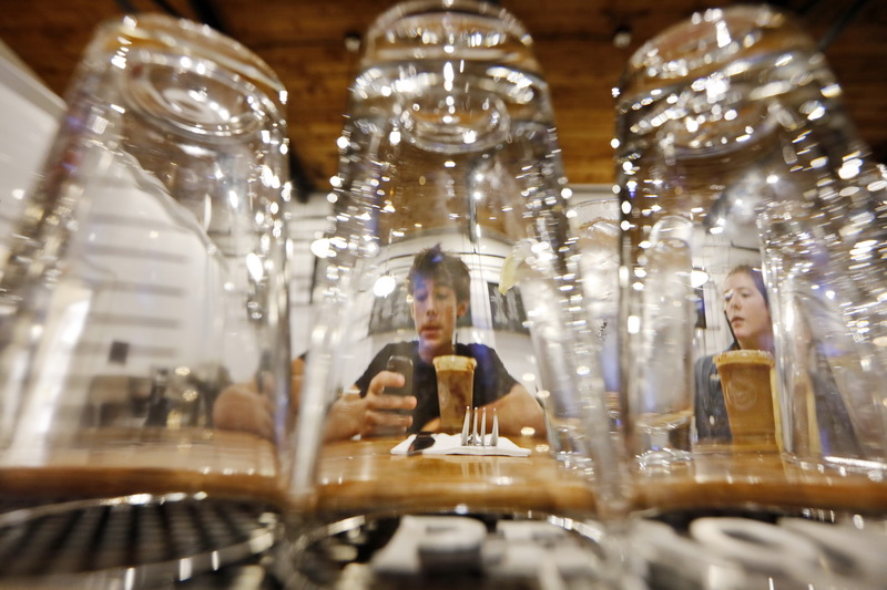 Julian Sudofski, center, and his sister Sofia Sudofski, right, enjoy a Chai Bomb for the first time, as seen through the glasses at the bar of the new opened Walrus & Captain restaurant in Mattapoisett, MA.