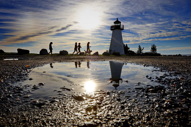 Joggers make their way past the Ned's Point Lighthouse in Mattapoisett, MA on a crisp morning.  The puddle betrays the recent rainfall we have had across the region.    PHOTO PETER PEREIRA