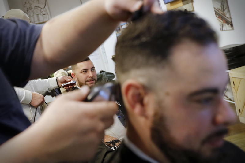Gunner Sinagra gets his weekly cut seen throught the arms of barber Jacob Henriques giving Gerry Conterno a fresh cut at the New Bedford Barber Co. on William Street in New Bedford. PHOTO PETER PEREIRA