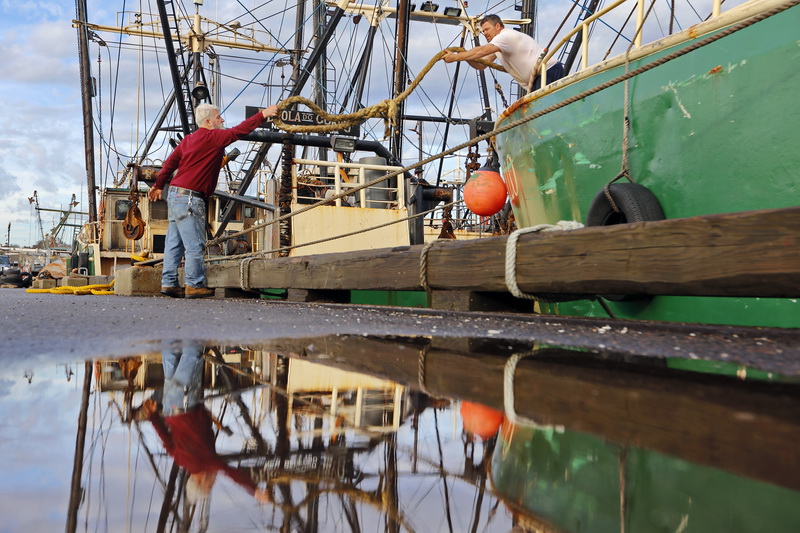 John Machie gives his son and captain of the fishing boat Apollo, Shawn Machie, a hand in undoing the lines as they prepare to cast off from New Bedford harbor.  PHOTO PETER PEREIRA