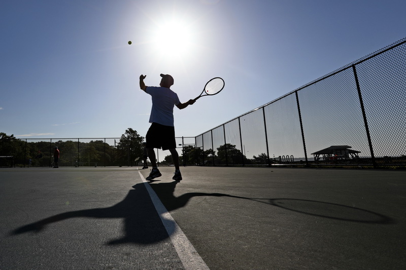 Ed Rose's shadow plays along, as he casts the ball into the air, while serving during a tennis match with friends at Fort Phoenix in Fairhaven, MA on a hot morning.  PHOTO PETER PEREIRA