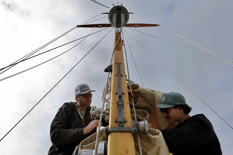 Ben Sperry and Nolan Clark of Sperry Sails install the sail they cleaned and repaired on a boat docked in Mattapoisett, MA. PHOTO PETER PEREIRA