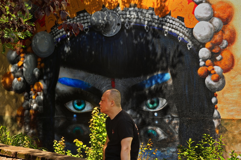 A mural painted on the side of a building keeps its eyes on a man sitting at Wings Court in New Bedford, MA on August 31, 2026. PHOTO PETER PEREIRA