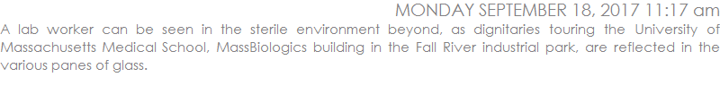 A lab worker can be seen in the sterile environment beyond as dignitaries touring the University of Massachusetts Medical School, MassBiologics building in the Fall River industrial park are reflected in the various panes of glass.