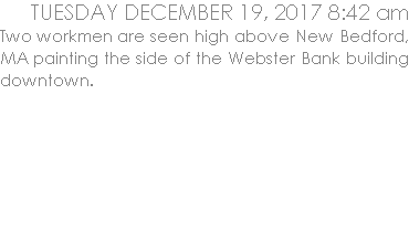 Two workmen are seen high above New Bedford painting the side of the Webster Bank building downtown.