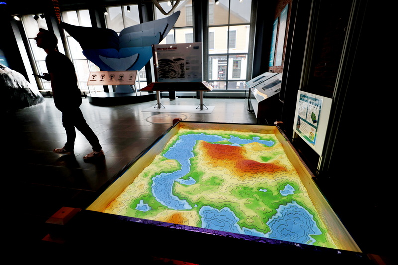 A visitor to the New Bedford Whaling Museum walks past the new Shaping Watersheds display which features real sand with a colorful computer overlay projected on it.  The sand can be moved with one's hand and the computer will calculate the impact the changes in terrain will have on water flow and environment. PHOTO PETER PEREIRA