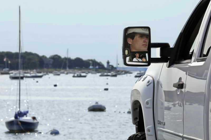A man is seen reflected from the mirror of his truck as he takes in the view of the harbor in Mattapoisett, MA.  PHOTO PETER PEREIRA