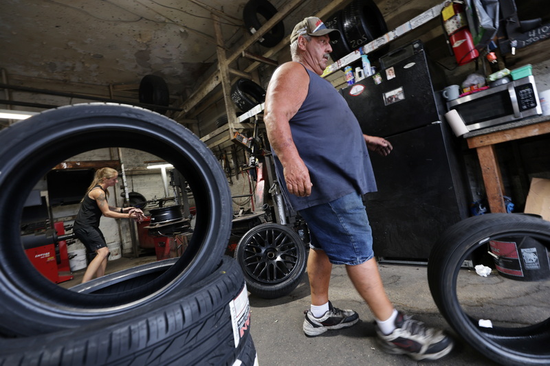 Dave Medeiros, manager, kicks a tire he removed from a wheel as Molly McGee prepares the wheel for a new tire seen in the foreground at Joe's Tire in New Bedford, MA. PHOTO PETER PEREIRA