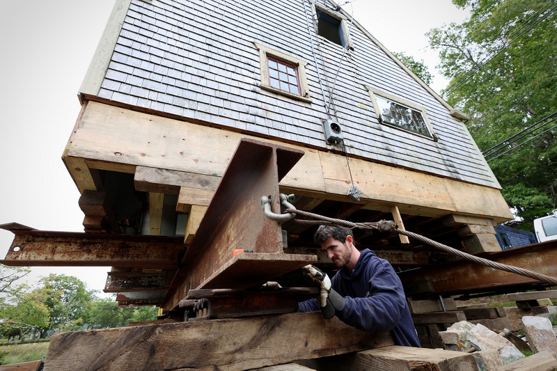 Jack Gordon of Gordon Building Movers, installs a slider under one of the beams during the moving of a historic house in Dartmouth, MA. Gordon Building Movers are in the process of relocating the 300-year-old house on Horseneck Road in Dartmouth to the left of its current location before bringing it back onto a new, elevated foundation. PHOTO PETER PEREIRA