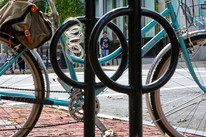 A man walking up Purchase Street in New Bedford is framed by the circular elements of a bike rack and bike tied up in front of the Green Bean Cafe on Union Street. PHOTO PETER PEREIRA