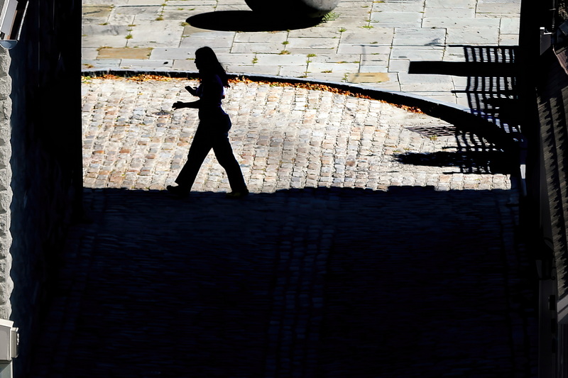 A woman walks along the line between dark and light at the bottom of Rose Alley in New Bedford, MA. PHOTO PETER PEREIRA