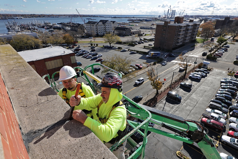 Edgardo Contrero and Joe Lopes are high above New Bedford as they make repairs to the rubber seals between the masonry work on top of the DeMello International Center in New Bedford, MA. PHOTO PETER PEREIRA