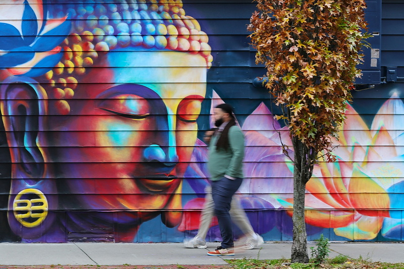 Two men walk briskly past the mural of Buddha meditating painted, on the side of the Spicy Lime restaurant on Pleasant Street in New Bedford, MA. PHOTO PETER PEREIRA