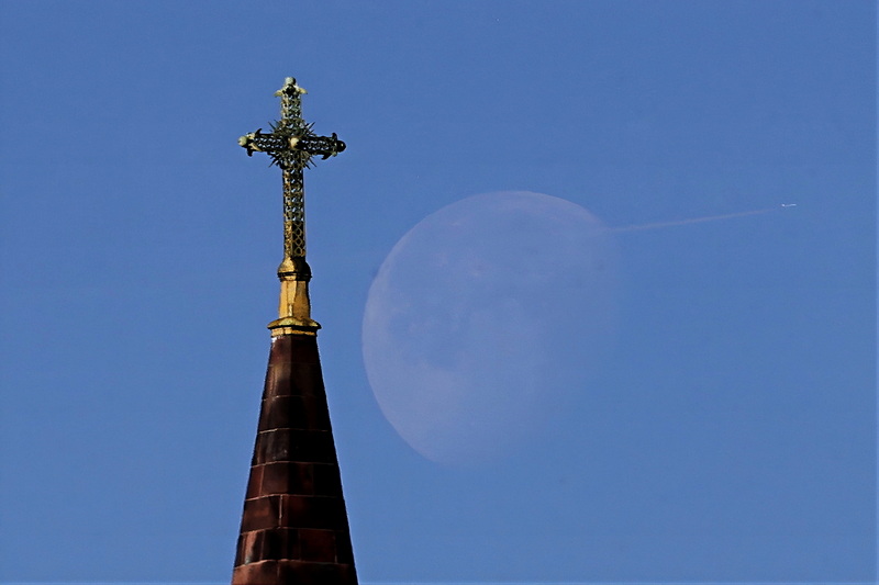 A plane makes its way across the setting moon in the background with the cross atop the St. Anthony of Padua Church on Acushnet Avenue in New Bedford, MA in the foreground, as seen from Market Basket parking lot. PHOTO PETER PEREIRA