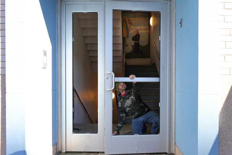 James Burbank of Silver City Glass checks the alignment of the custom doors he is installing at Our Lady's Chapel in New Bedford, MA.  In the background a mural of a Franciscan friar praying to Our Lady. PHOTO PETER PEREIRA