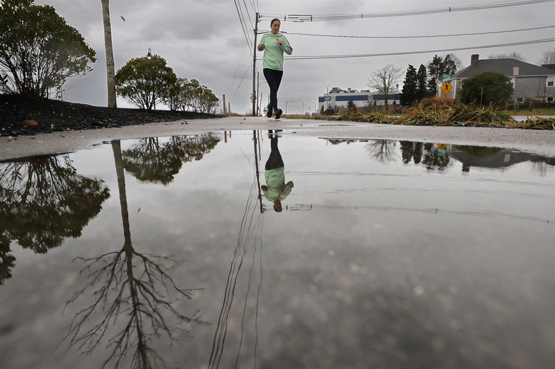 A woman jogging down East Rodney French Boulevard in New Bedford, MA is mirrored in a puddle while heavy rain falls across the region. PHOTO PETER PEREIRA