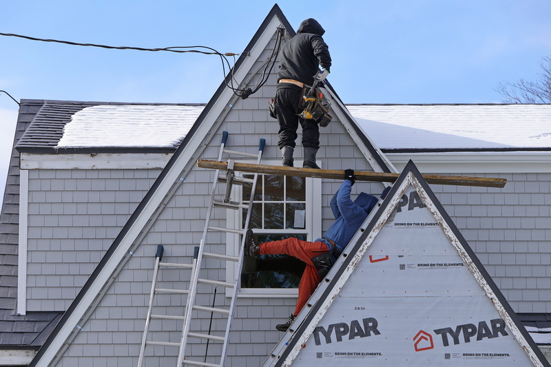 In Dartmouth, MA, two carpenters assist one another to climb to the peak of the home's A-frame while installing vinyl siding. PHOTO PETER PEREIRA