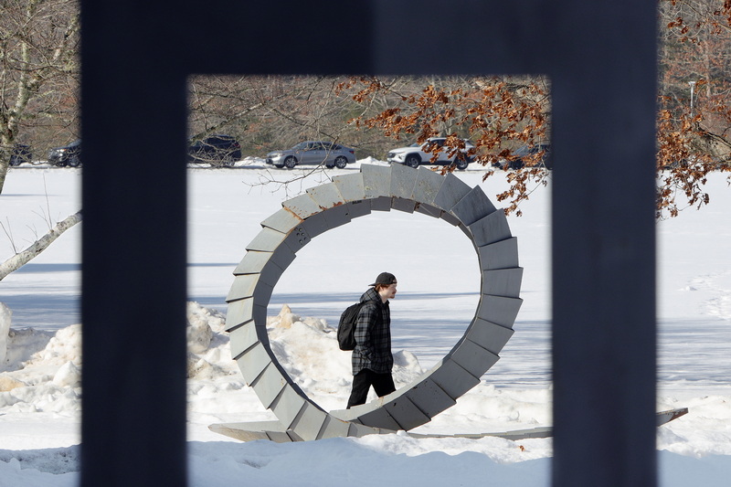 A UMass Dartmouth student is framed by two sculptures outside of the CVPA center as he makes his way to class across a snowy landscape. PHOTO PETER PEREIRA