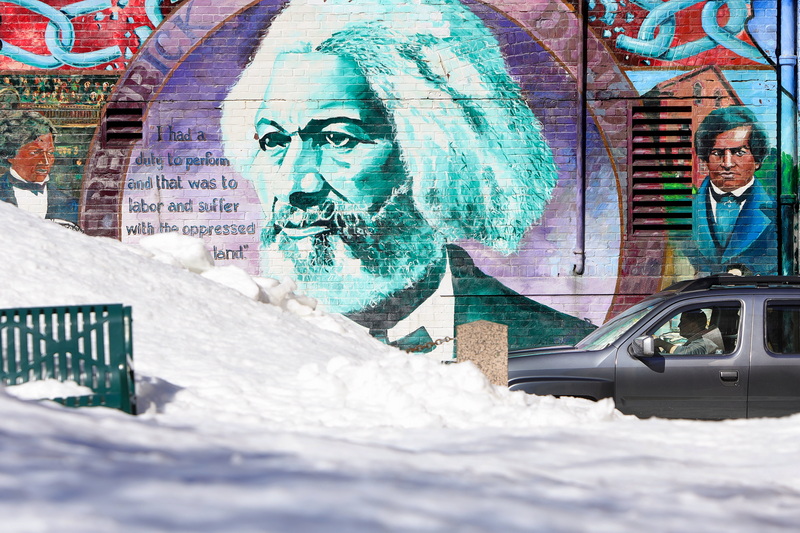 A motorist tries to drive out past the mural of Frederick Douglass painted on the side of a building in downtown New Bedford, MA partially obscured by a giant snow pile. PHOTO PETER PEREIRA
