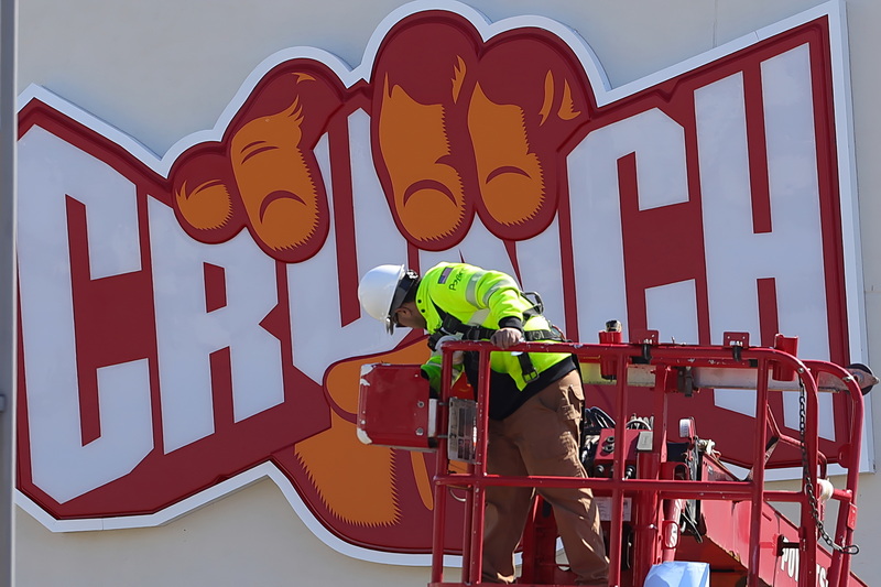 A Poyant Signs technician is seemingly being crunched by a giant hand on the sign he is installing in front of the new Crunch Fitness gym on West Rodney French Boulevard in New Bedford, MA. PHOTO PETER PEREIRA