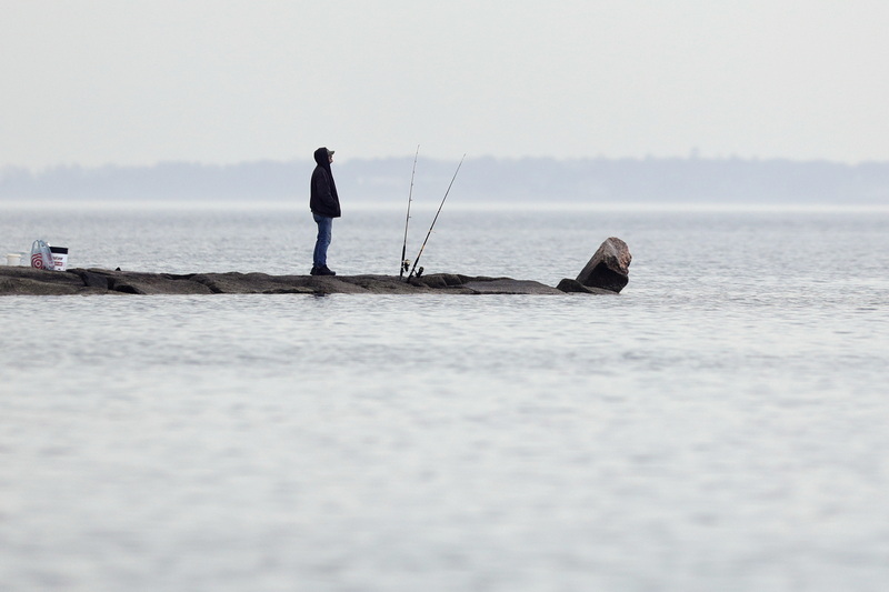 A man looks to the heavens as he waits for fish to bite as he fished from a jetty on East Beach in New Bedford, MA. PHOTO PETER PEREIRA