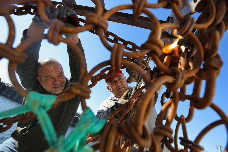 Chris Simpson puts tension on the chain as Jaime Lopez uses a cutter to loosen a stuck shackle on a dredge aboard a scalloper docked in New Bedford, MA.  PHOTO PETER PEREIRA